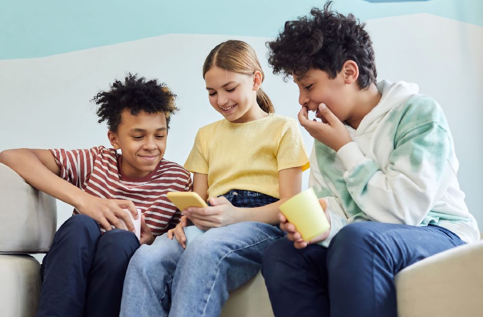 Three teenagers are enjoying each other's company while using smartphones indoors.