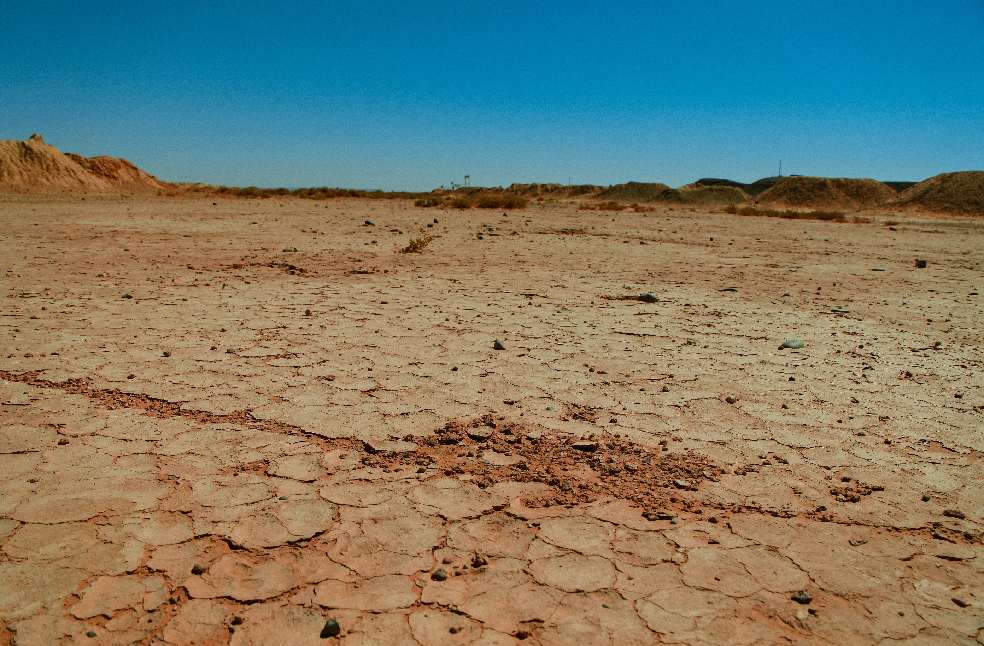 Dramatic view of a cracked, barren desert landscape under a clear blue sky with an arid environment.