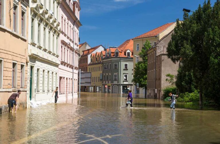 Catalonia flooding causes widespread disruption across Spain People navigating a flooded street in a European town on a sunny day.