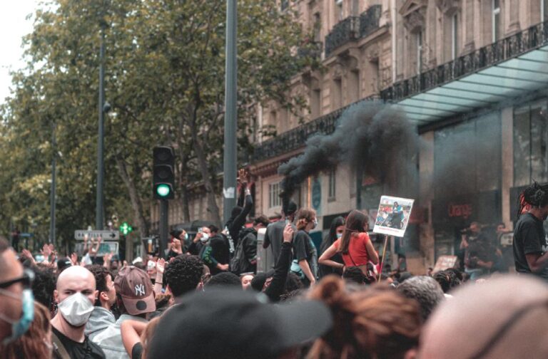 France protests fuel violence across cities with mass arrests Diverse group protesting outdoors with banners and smoke in urban environment.