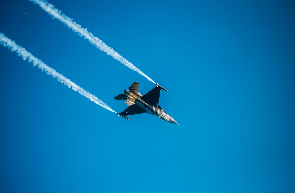 A dynamic image of a jet fighter soaring through a clear blue sky, leaving vapor trails.