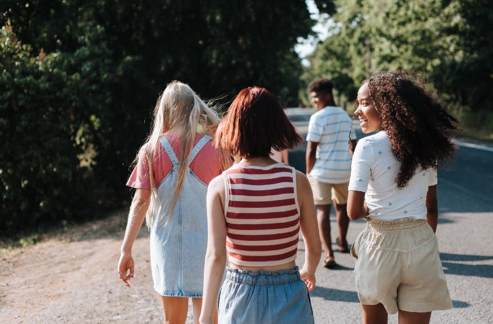 A diverse group of teenagers walking happily in the summer along a tree-lined road.