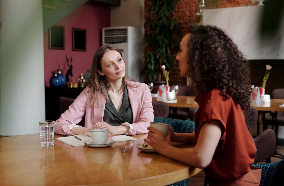 Two women having a thoughtful conversation over coffee in a stylish indoor café setting.