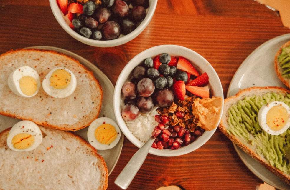 A fresh and vibrant breakfast flat lay featuring a yogurt bowl with fruits and toast with eggs and avocado